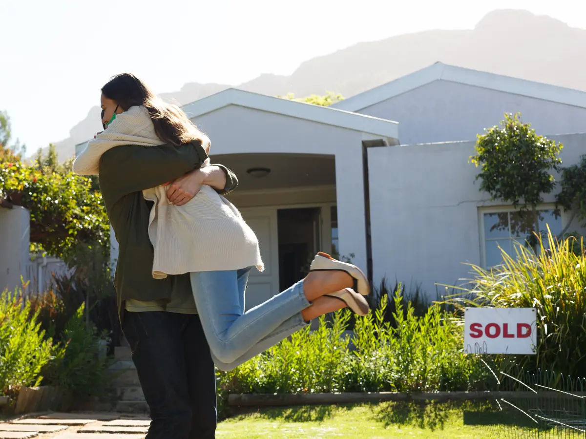 Couple hugging in front of their home with a SOLD sign in the yard