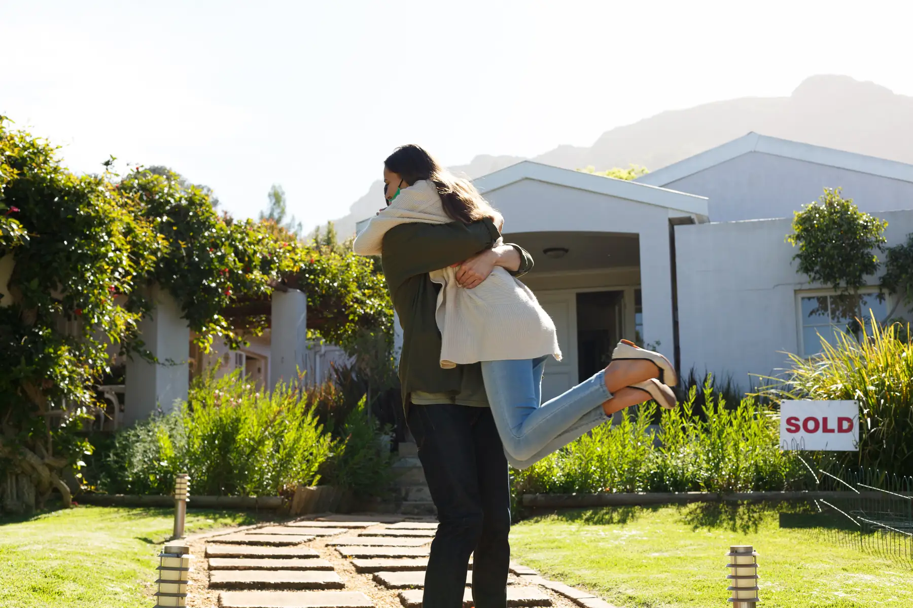 Couple hugging in front of their home with a SOLD sign in the yard
