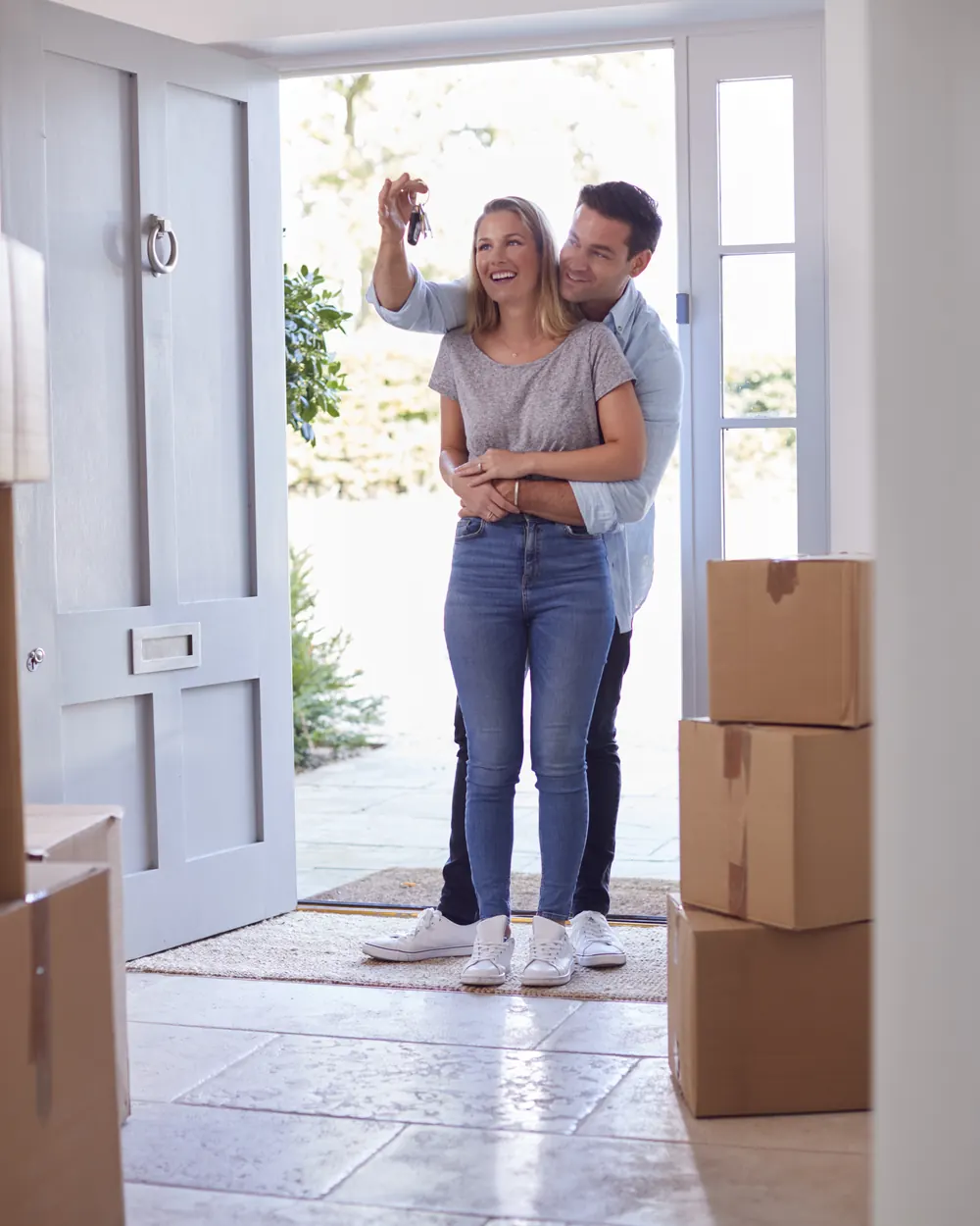 New homeowners holding up their keys in the doorway beside moving boxes