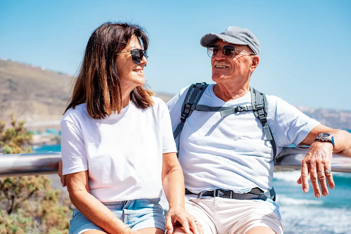Smiling couple in their sixties sitting together above the ocean on the California coast