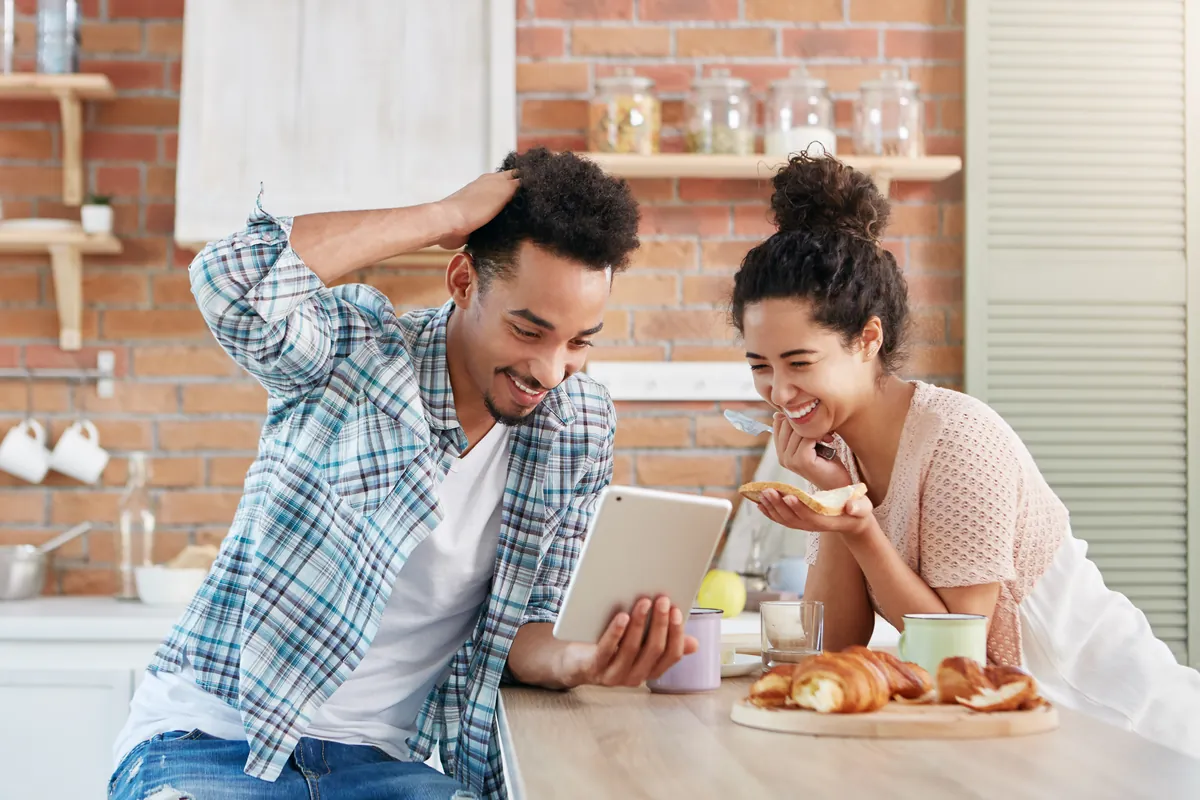 Smiling couple at their kitchen counter checking their home value on a tablet