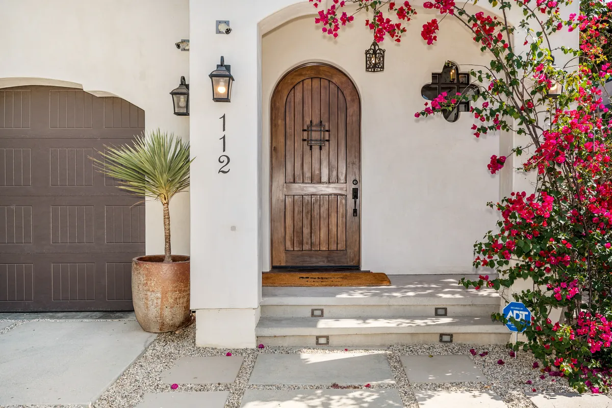 Arched wood front door with potted palm, bougainvillea and house numbers
