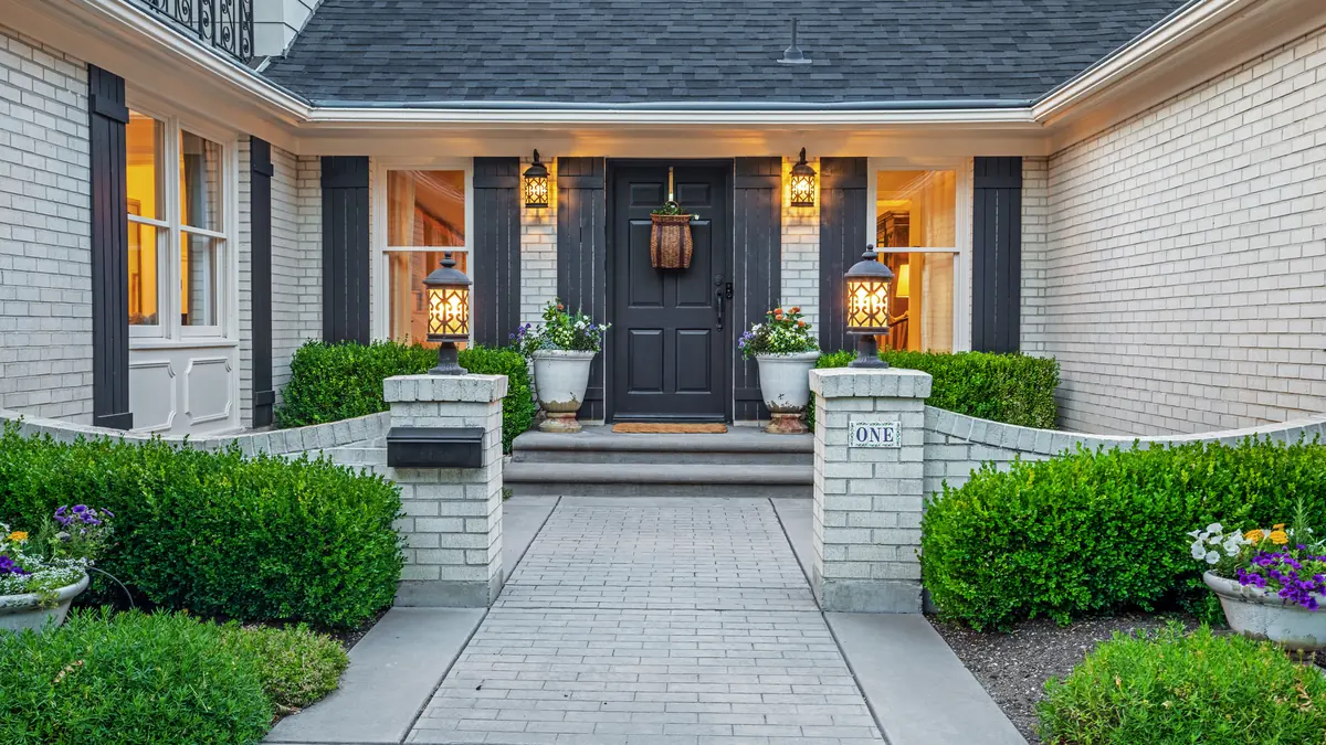 Inviting front entrance of a home with a brick walkway, trimmed hedges and warm porch lights