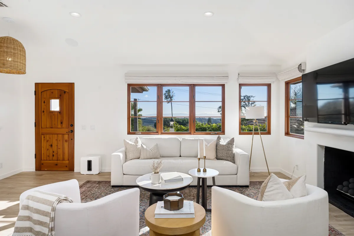 Bright staged living room with white sofas, neutral decor and windows to a view
