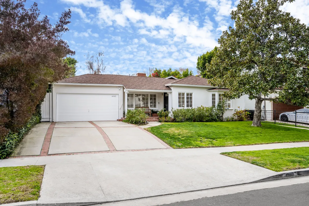 Single level home with a green lawn and a wide driveway under a blue sky