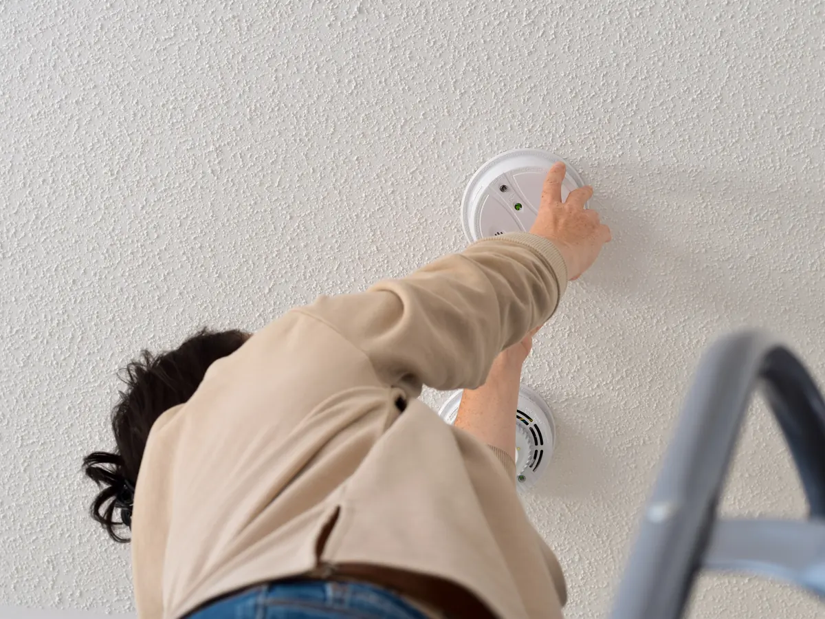 Homeowner installing a smart smoke and carbon monoxide alarm on the ceiling