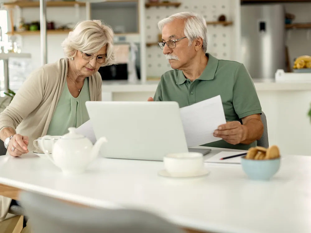Senior couple at a kitchen table reviewing a document together beside a laptop